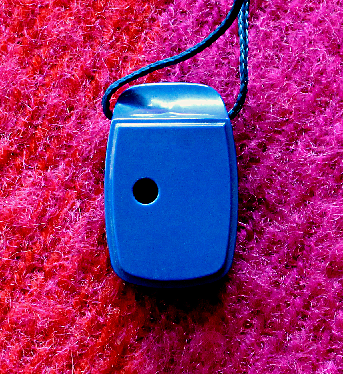Back of a blue ocarina showing the thumb hole, laying on a red wool background.
