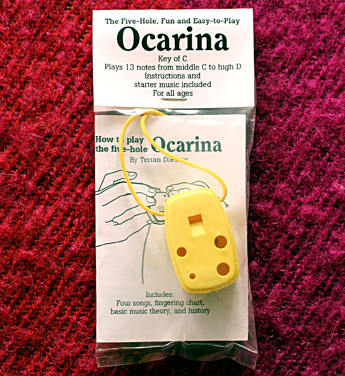 Front side of a yellow ocarina with instruction booklet.